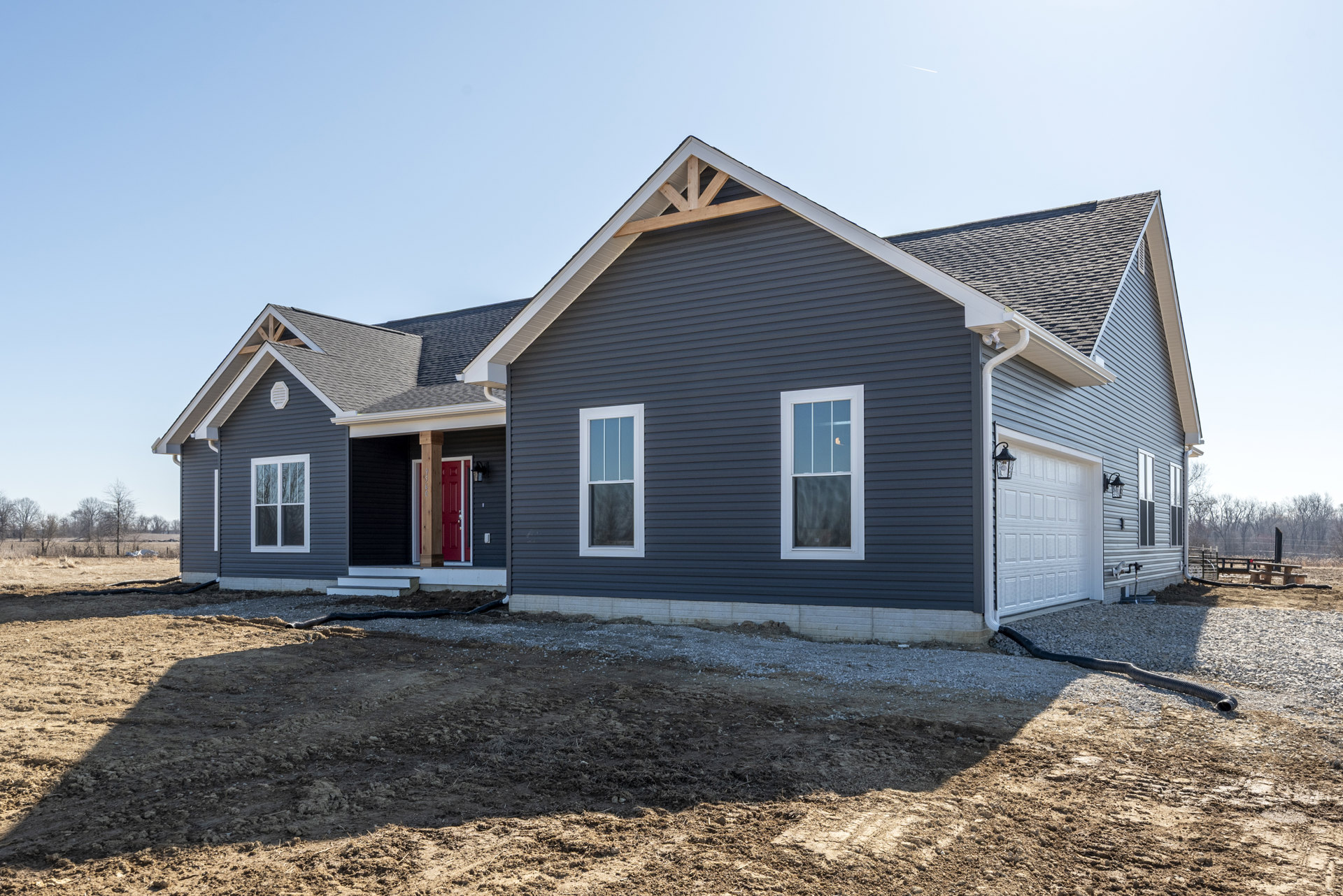 Two-story house with white siding, red front door, multiple windows with white frames reflecting light, paved driveway, and dirt patch near the foundation