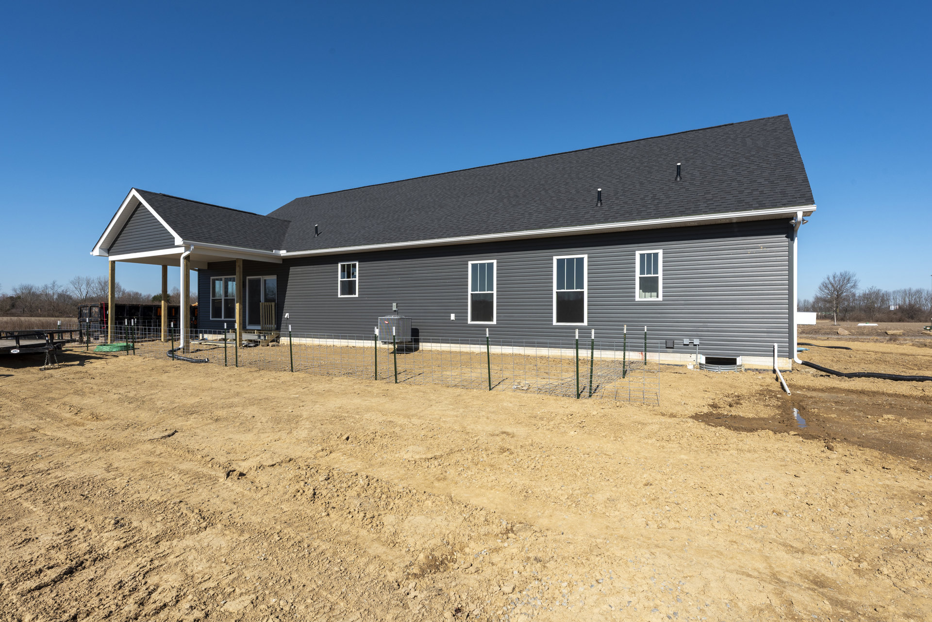 Two-story house with white-framed windows, fenced dirt yard, and surrounding trees on a spacious lot
