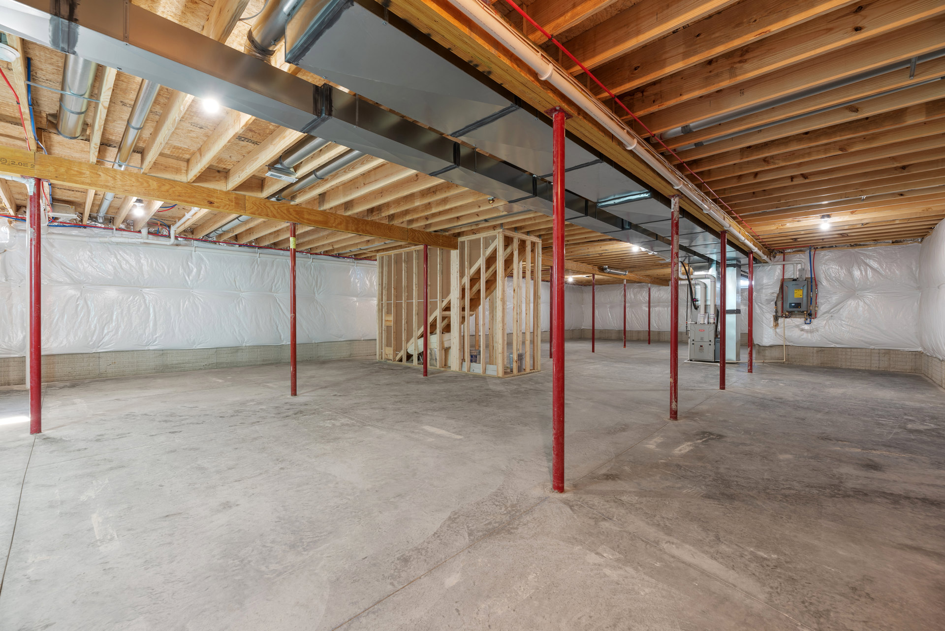 Basement room with exposed wooden ceiling, red structural poles, concrete floor, metal beams, and visible pipes.