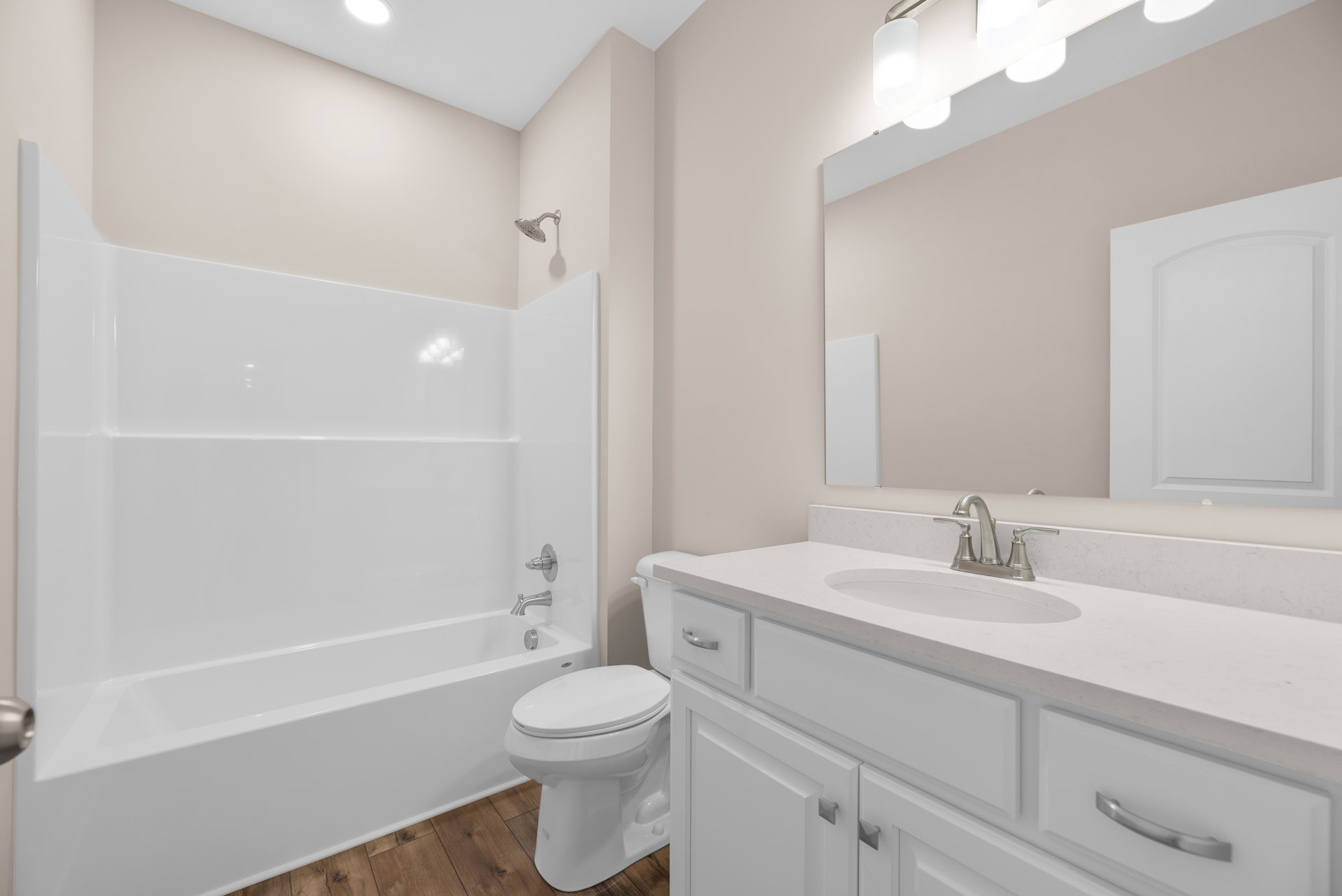 White bathtub and toilet beside a white vanity with chrome faucet, light tile flooring, and curved-top door in a bright bathroom.