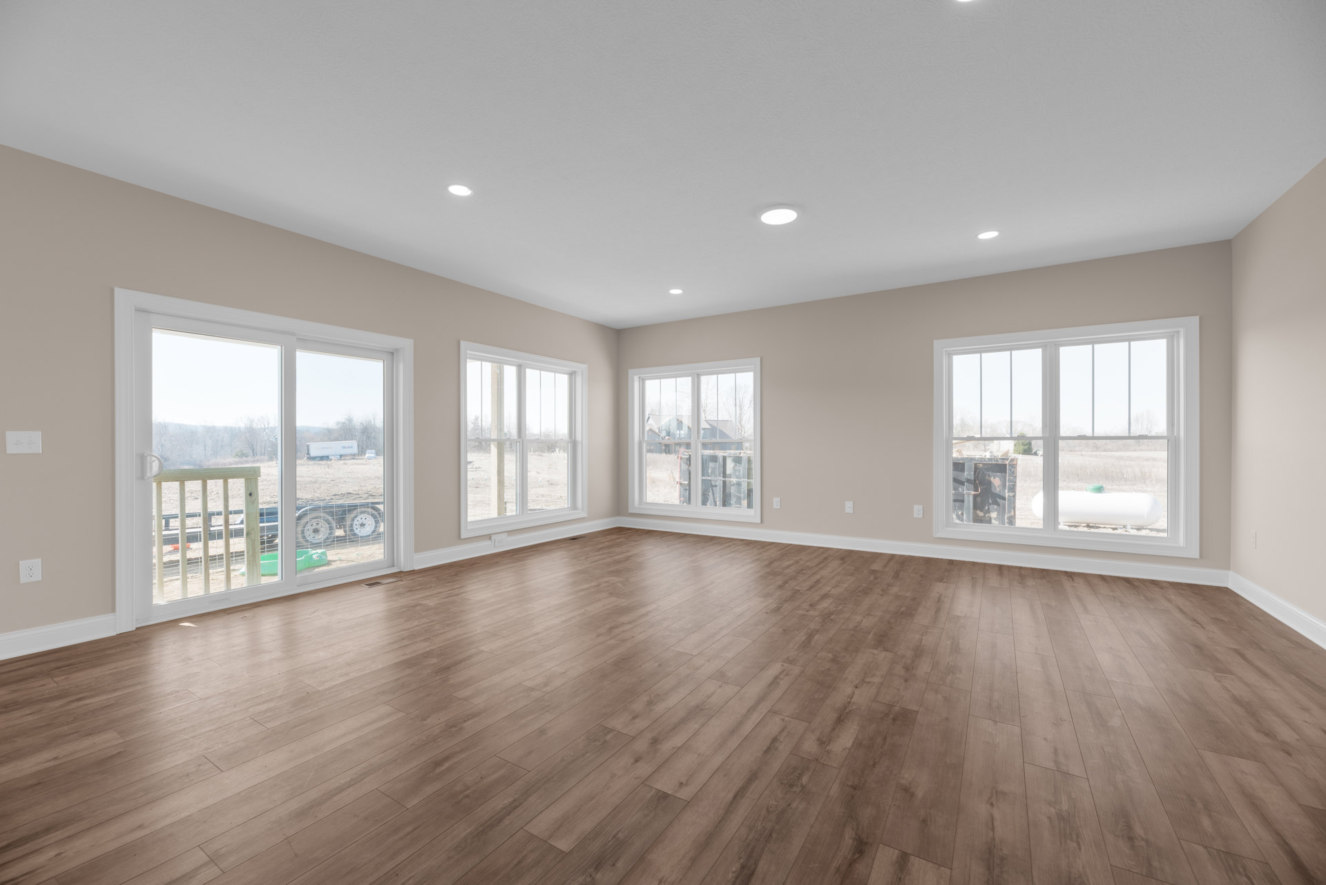 Spacious room featuring hardwood floors, large windows with outdoor views, white walls, and ceiling
