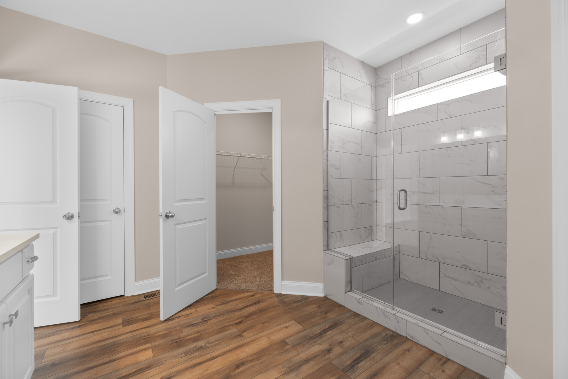 Bathroom featuring a glass shower enclosure, white paneled doors with silver knobs, wood flooring partially covered by a light carpet, white cabinetry, and an open closet with