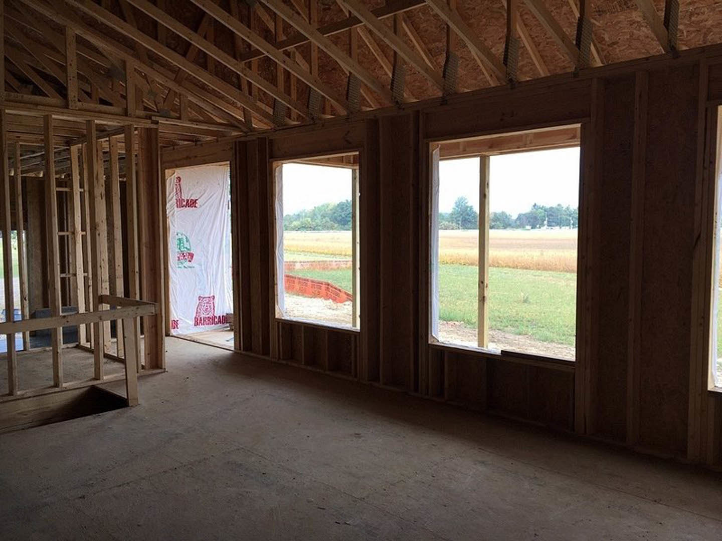 Spacious room featuring large windows overlooking an open field, light wood flooring, exposed ceiling beams, and neutral walls.
