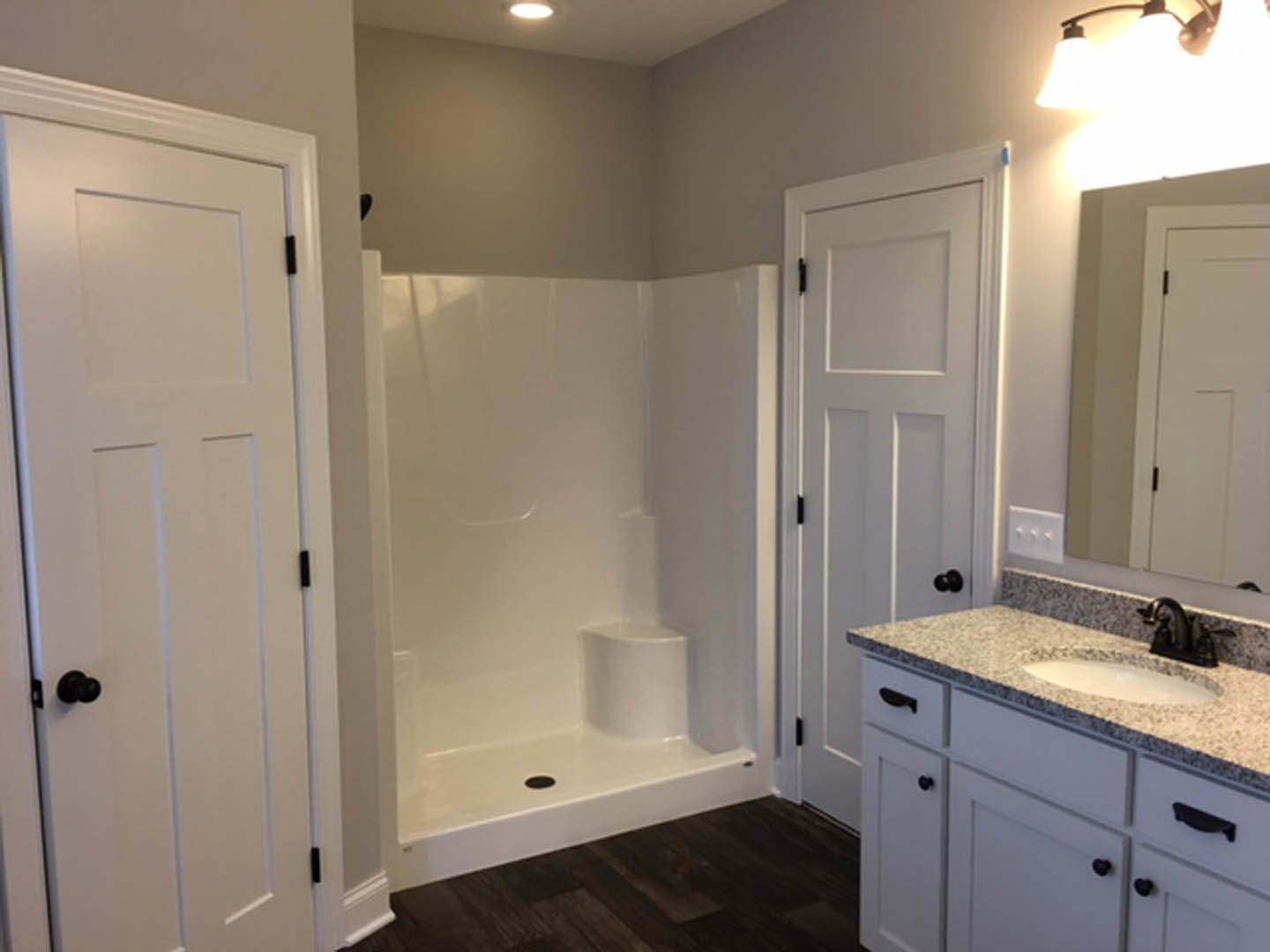 White bathroom with tile shower stall, glass door, white vanity cabinet with black handles, dual light fixture above sink, and white walls.