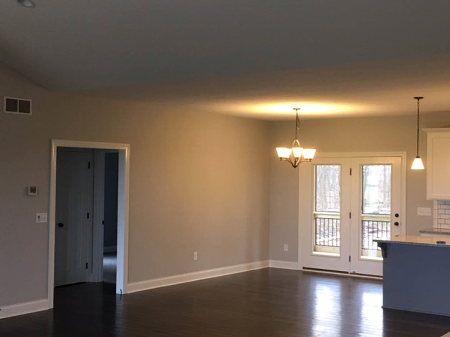 White double doors with black handles, glass window panels, light laminate flooring, white plaster walls, and a modern chandelier hanging from the ceiling.