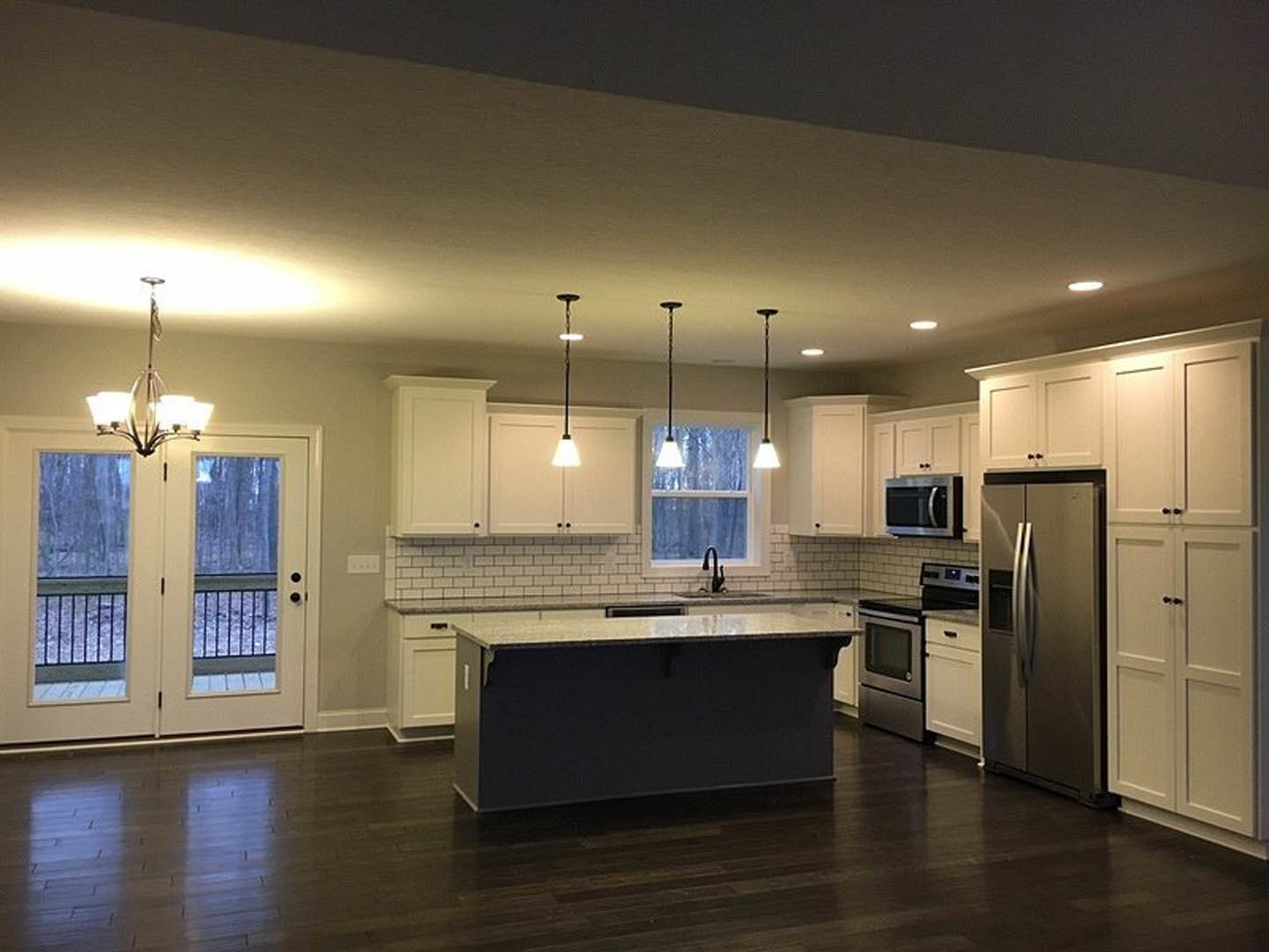 Spacious kitchen featuring a large central island with white countertop, shaker-style cabinetry, stainless steel refrigerator, built-in microwave with handle, double glass-paneled