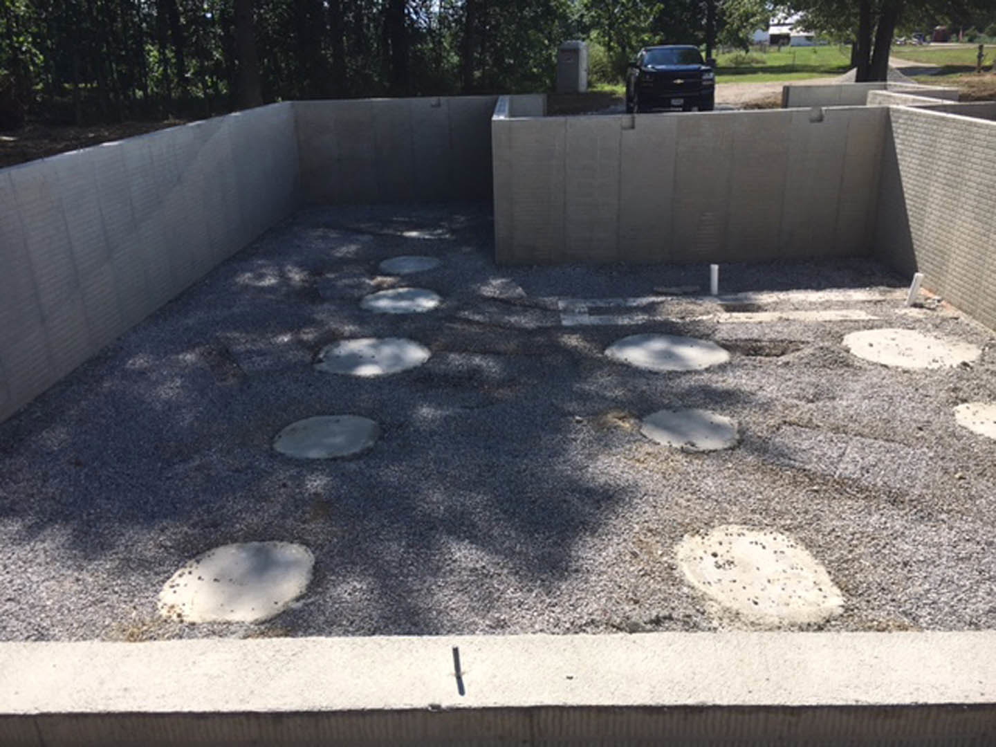 Concrete foundation with embedded circular stones, surrounded by outdoor landscaping and trees.