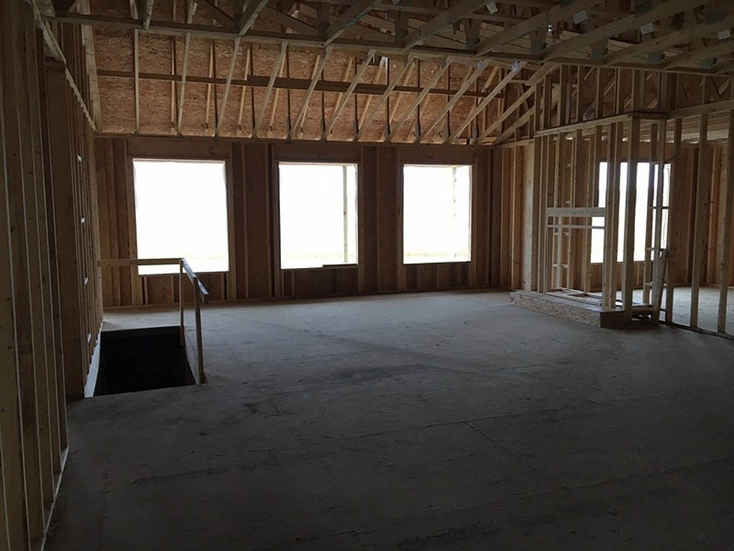 Open-concept room featuring a wood staircase, white walls, exposed ceiling beams, rectangular window with white frame, and natural daylight illuminating hardwood floors.