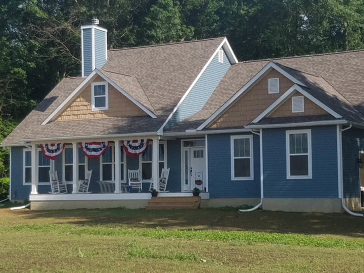 Two-story house with light siding, covered front porch, white-framed windows, manicured lawn, and mature trees in the yard
