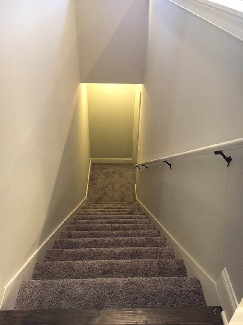 Carpeted staircase with wooden handrail ascending toward a plaster wall illuminated by a ceiling light