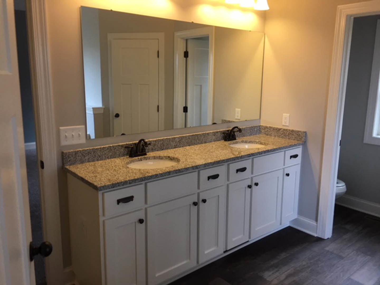 Bathroom with expansive wall mirror, white countertop, chrome faucet, light switch, and wood cabinetry
