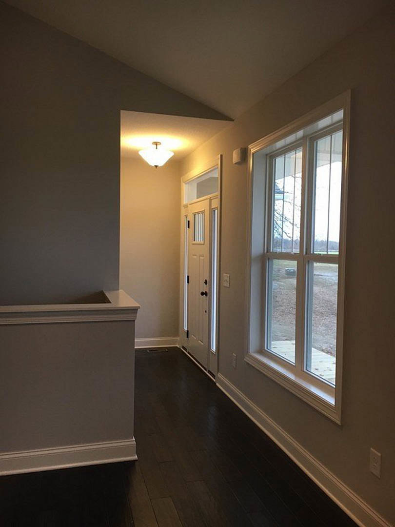 Hallway with dark wood flooring, white walls, white door with black knobs, window showing outdoor view, ceiling light fixture, decorative molding