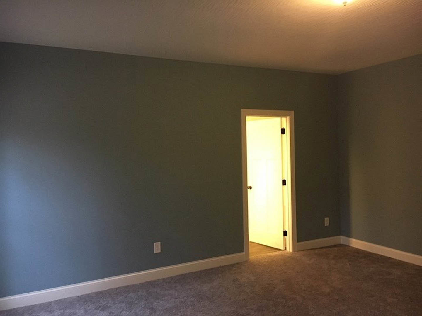 White door open to carpeted room with blue accent wall, white ceiling, and lamp casting light across floor.