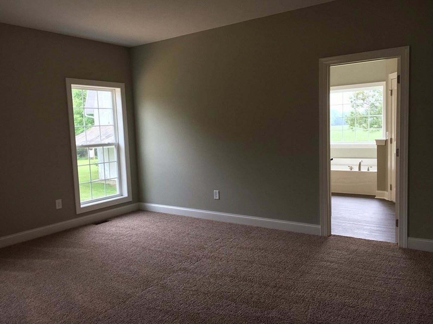 Open white door leading to a carpeted room with large window, plaster walls, and view of trees outside