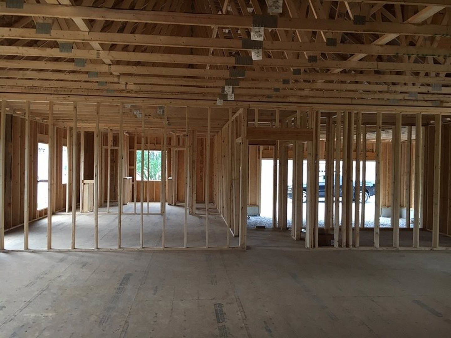 Wood framing and exposed beams in a partially constructed room with concrete floor, daylight streaming through unfinished windows