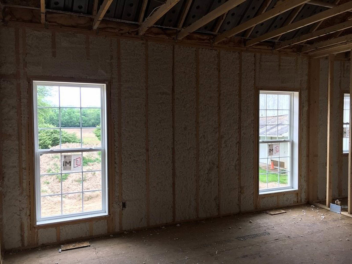 Vaulted ceiling with exposed wooden beams, large windows letting in daylight, neutral walls, and hardwood flooring