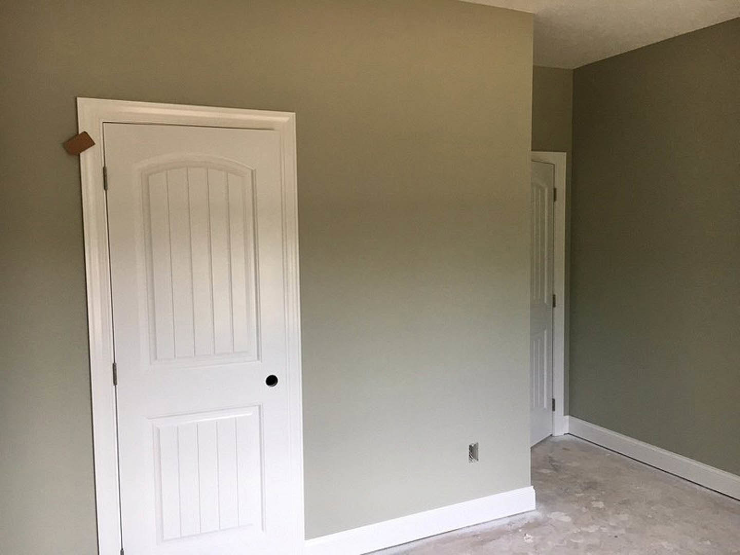 White interior door with metal handle set in plaster wall, concrete flooring visible in foreground.