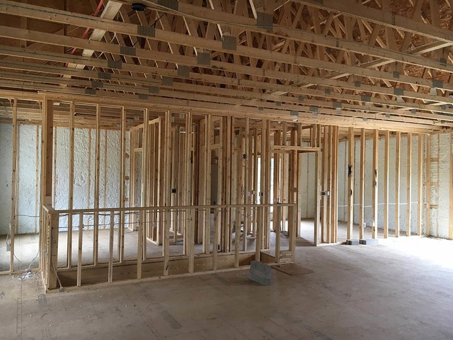 Wood-framed room under construction with exposed beams, unfinished walls, and grey brick resting on a table