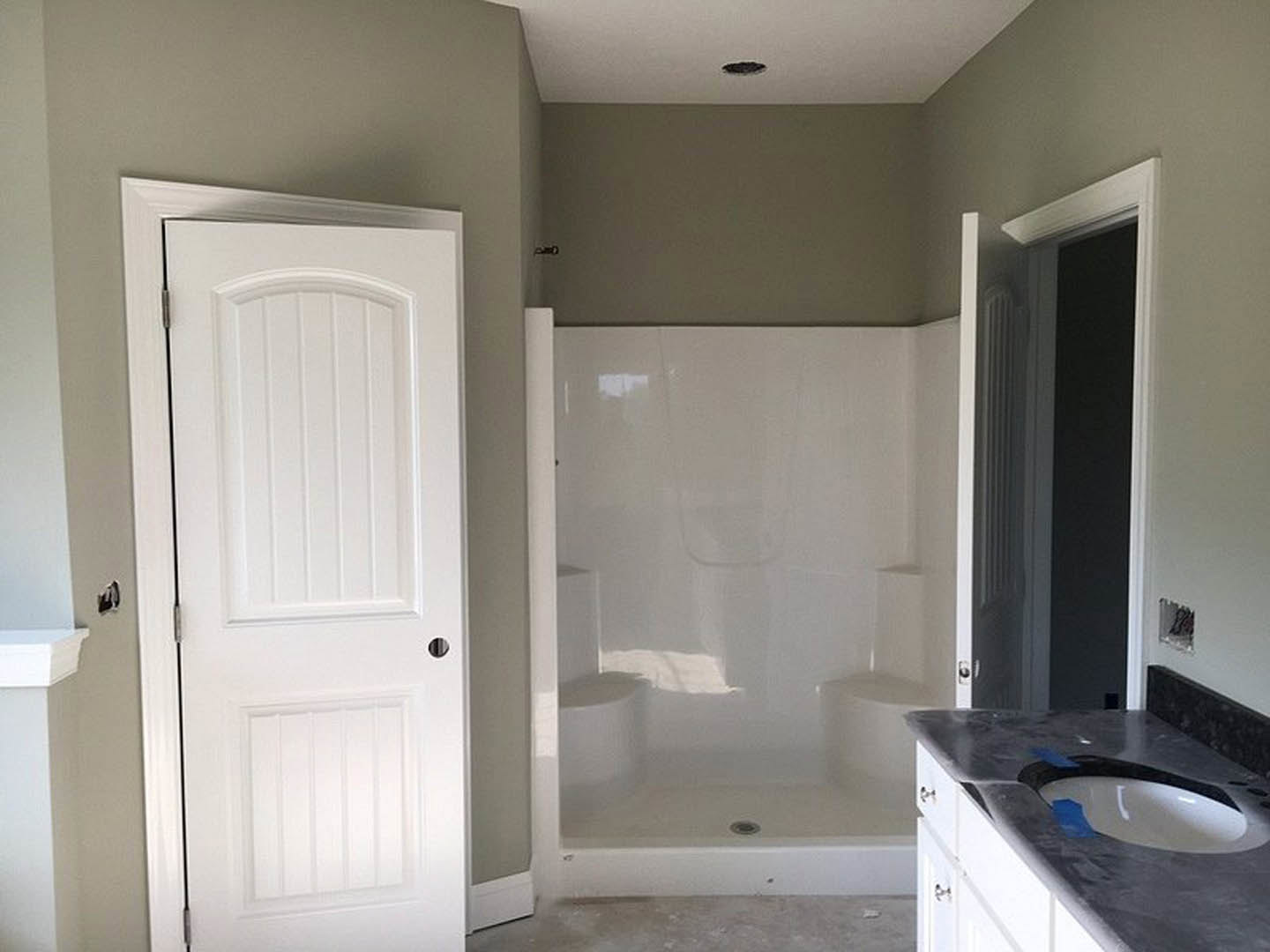 Bathroom with white tile shower, white sink set in a light-colored countertop, blue painter’s tape on sink, white door with round hole, neutral walls, chrome plumbing fixtures.