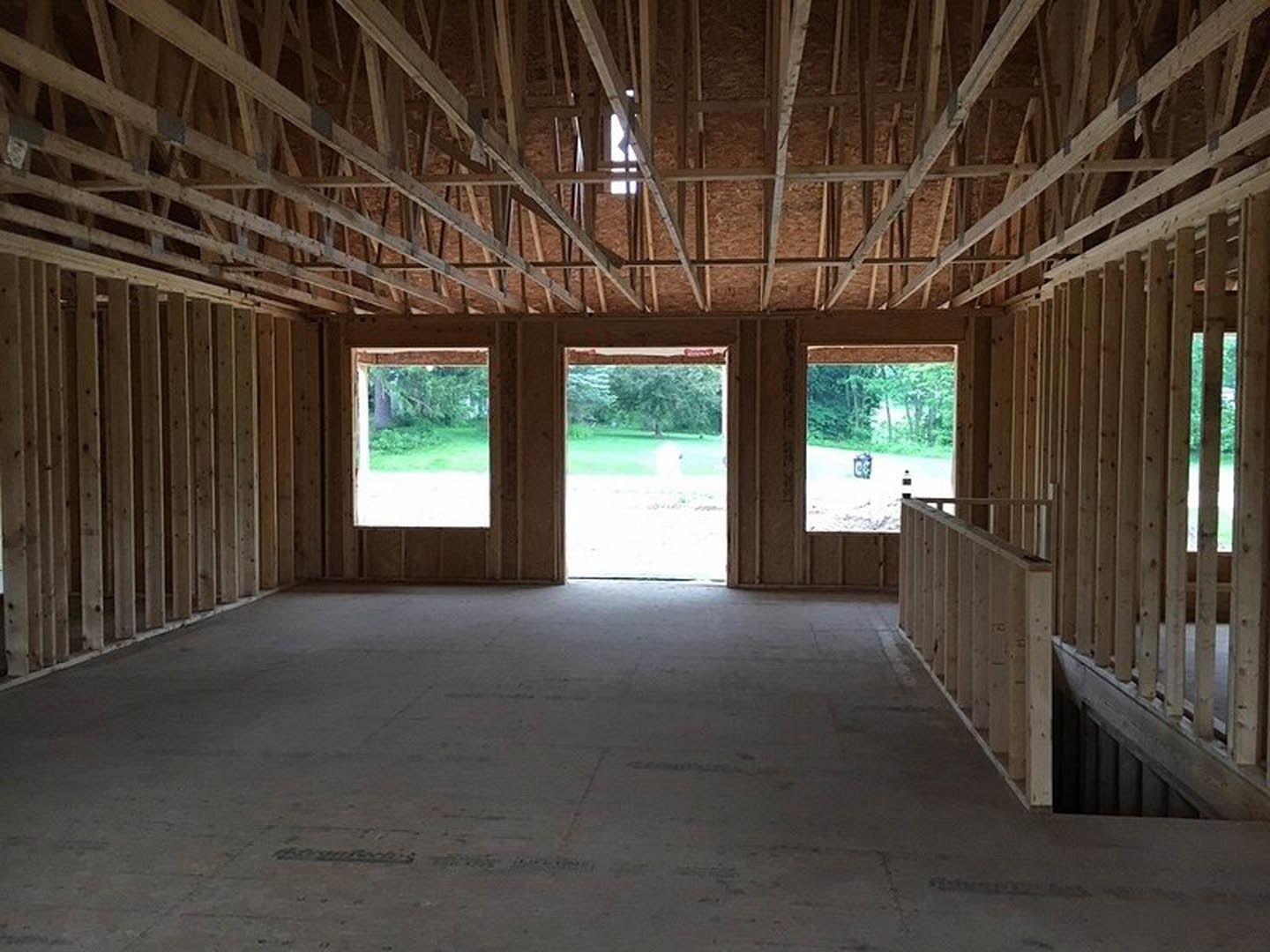 Open room with wood beam ceiling, large windows, concrete floor, and doorway leading to adjacent space