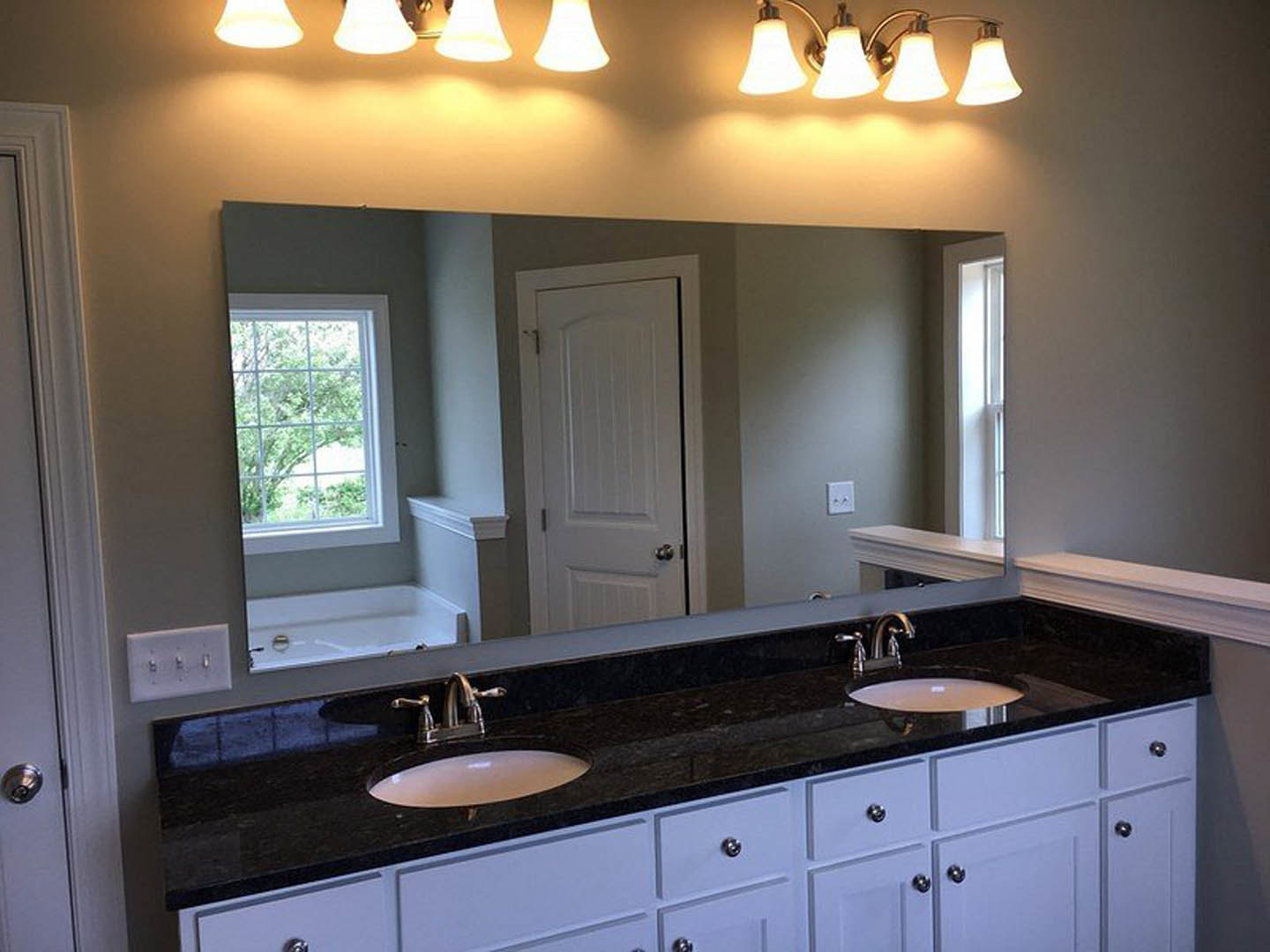 Bathroom with a wide framed mirror above a white countertop and sink, square-paned window, chrome faucet, tile backsplash, white cabinetry, and a white door with metal handle.