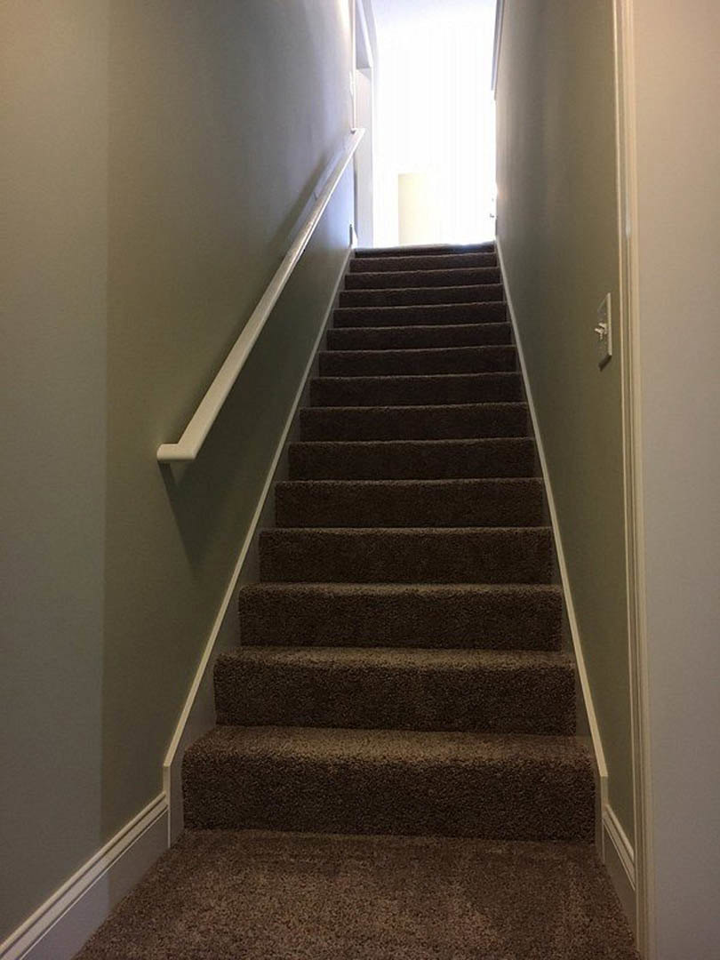 Carpeted staircase with wooden handrail, illuminated by sunlight streaming through narrow wall openings