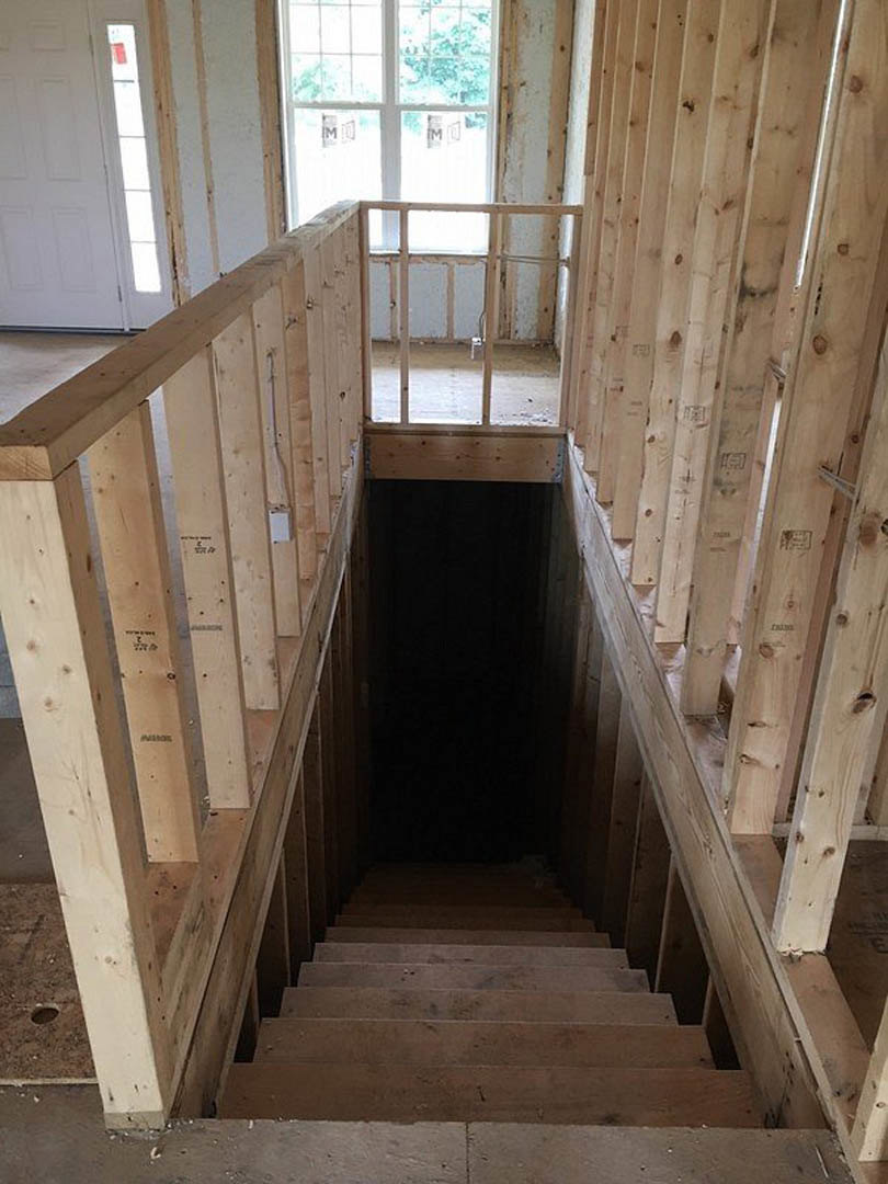 Wood staircase with white square-patterned door, window with white frame, plank flooring, and neutral walls in a residential interior.