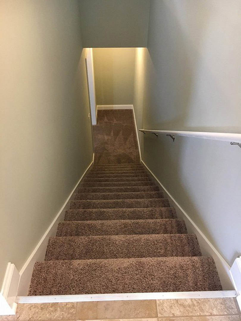 Carpeted staircase with wooden handrail, plaster walls, and neutral-toned flooring in a residential interior