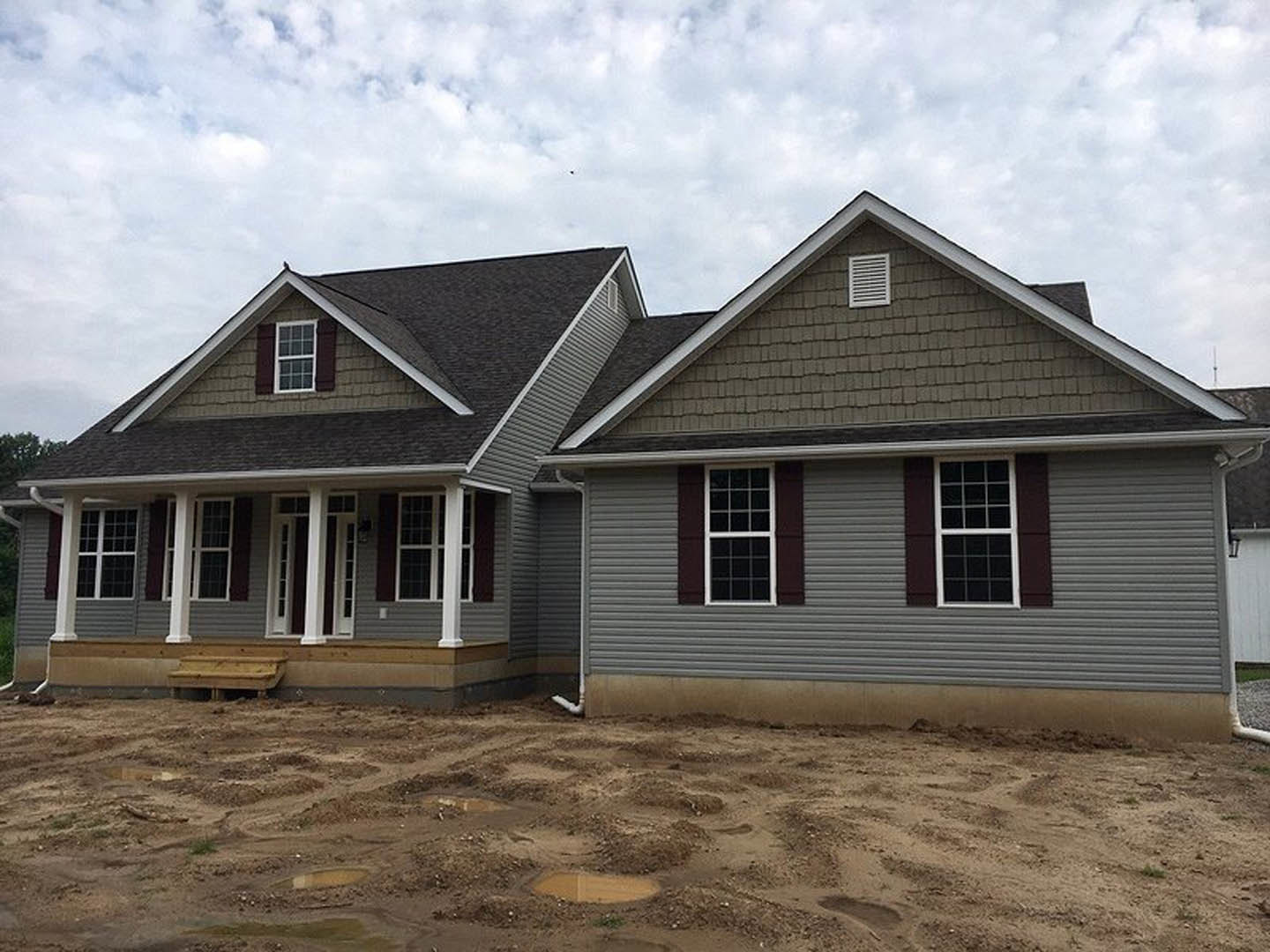 Grey-roofed house under construction with exposed wooden beams, dirt foundation, and visible exterior vents and siding
