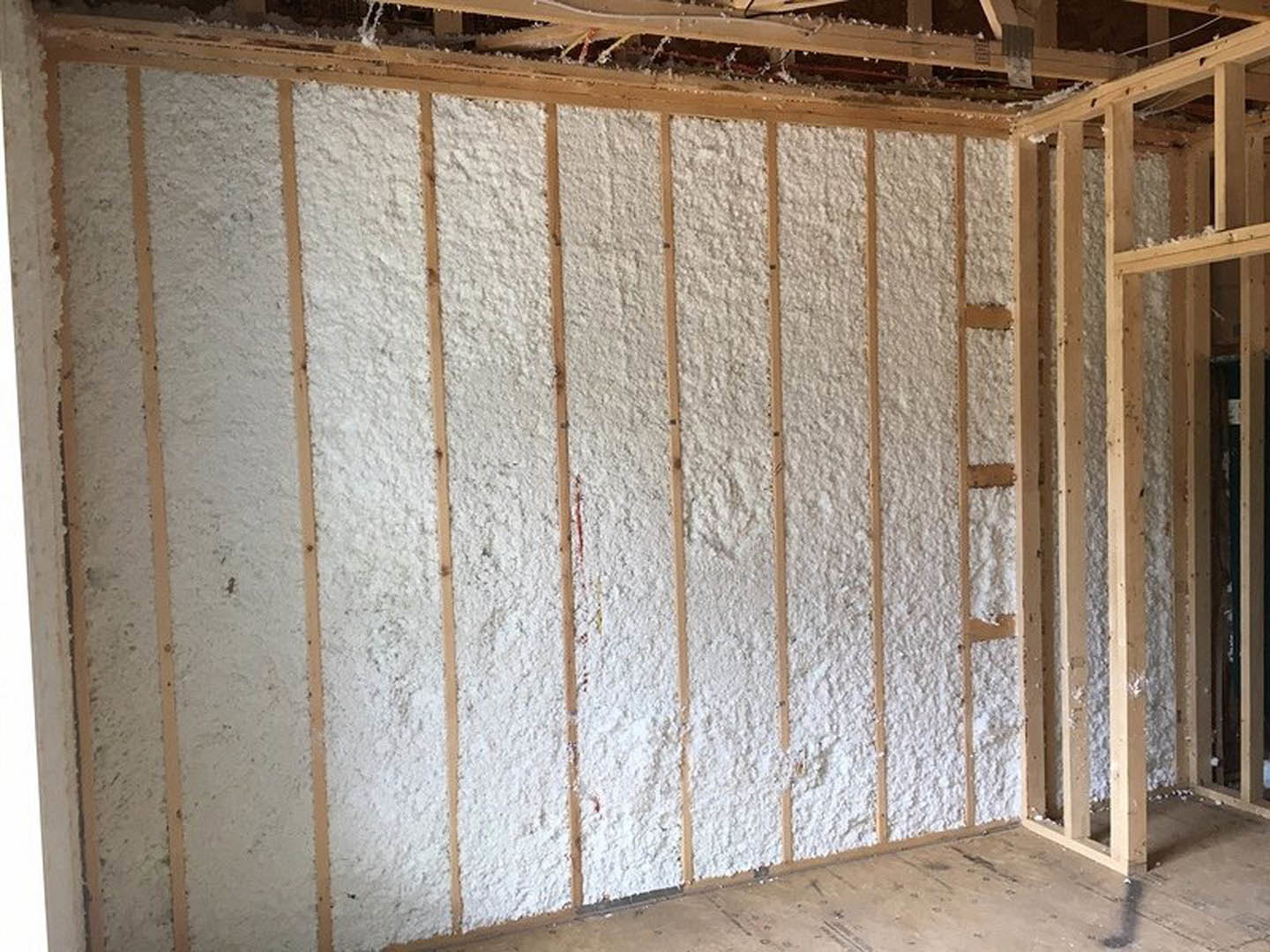 Spray foam insulation covering wall studs in unfinished room with exposed wood framing and construction materials