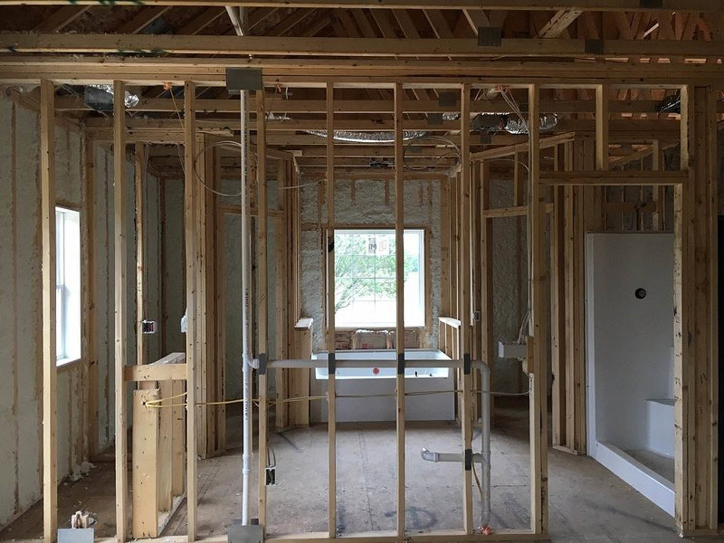 Freestanding bathtub beside a large window, white walls with built-in shelf, white bench featuring a red accent, natural light streaming through glass, black rectangular fixture