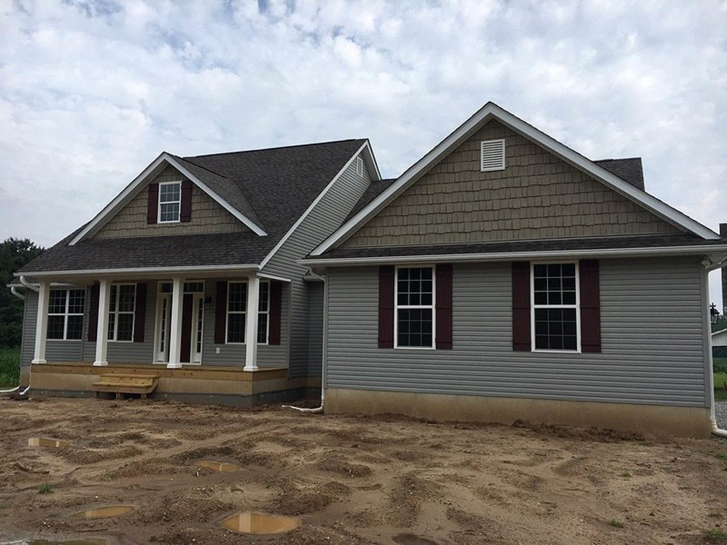 Partially built house with grey roof, exposed wood framing, metal siding, and dirt construction area in foreground