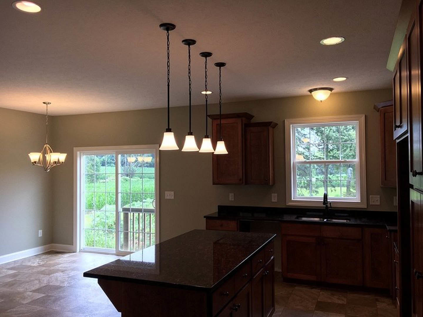 Modern kitchen featuring a central island with quartz countertop, pendant lights hanging from the ceiling, white cabinetry, hardwood flooring, and large windows overlooking a