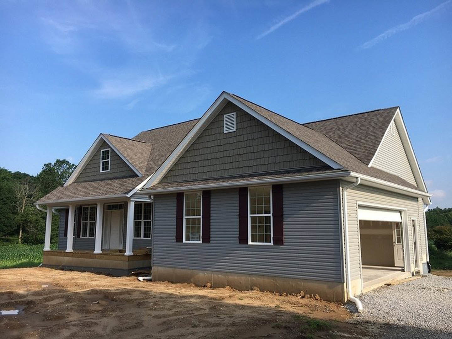 Partially built house with white framed windows, vent, white door with window, attached garage, gravel and wooden walkway, cloudy sky overhead