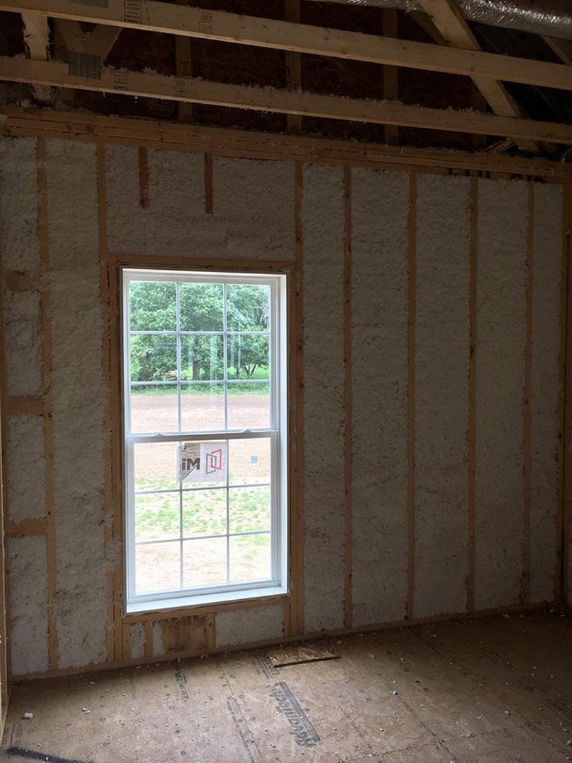 Large window with clear glass set in a wood-framed wall, natural daylight illuminating light plank flooring and exposed wooden ceiling beam, small sign visible on windowpane
