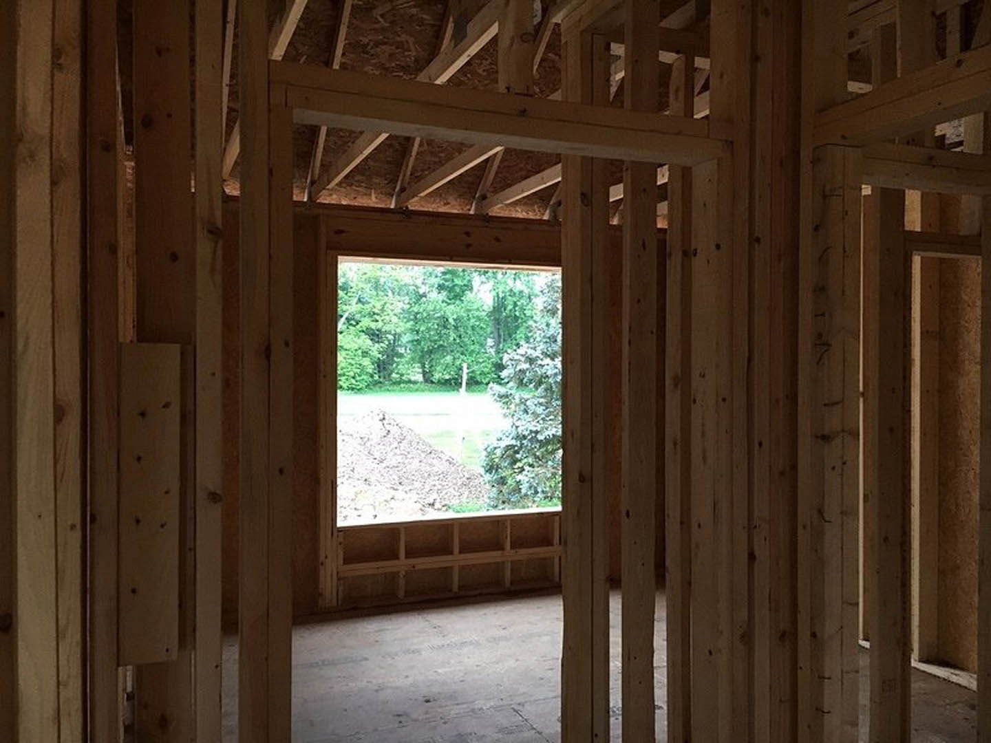 Bright room with wood plank ceiling, large window framing a view of grassy field and scattered rocks, light walls, and exposed wooden beams
