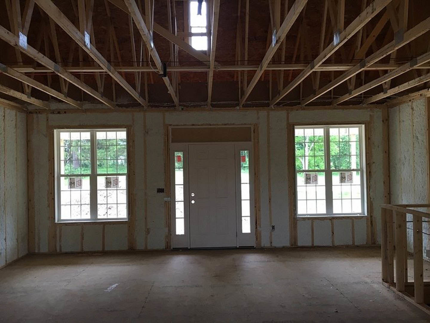 White interior room featuring a paneled door, multiple rectangular windows, exposed ceiling beams, and a smooth concrete floor.