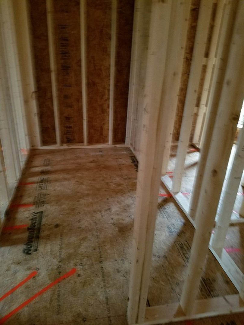 Wood framing and beams in a partially finished room, concrete floor marked with red lines, exposed insulation and plaster on walls
