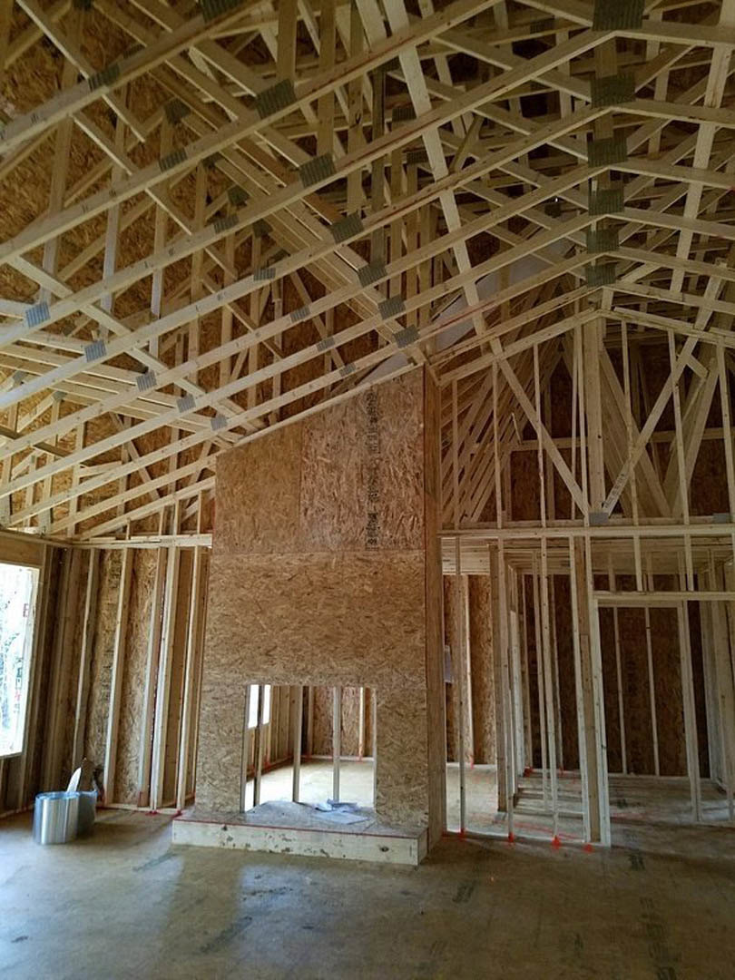 Exposed wood framing and beams forming interior walls and ceiling, concrete floor, window allowing natural light into unfinished space