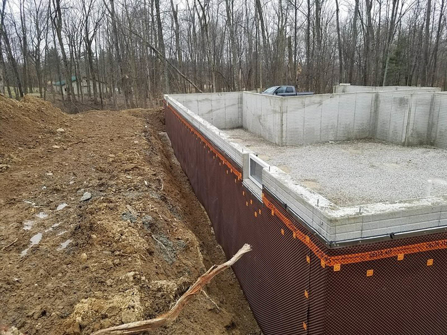Concrete foundation and metal retaining wall surrounded by dirt, with trees in the background and a parked car nearby