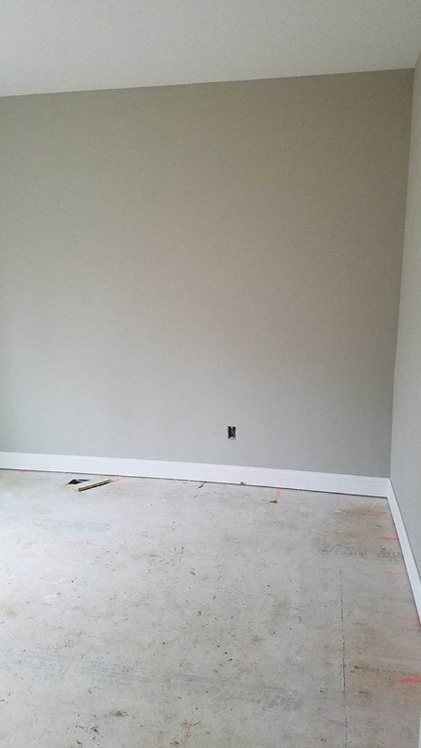 White plaster wall with a rectangular hole, exposed concrete floor, person standing on a wooden table in a partially remodeled interior.
