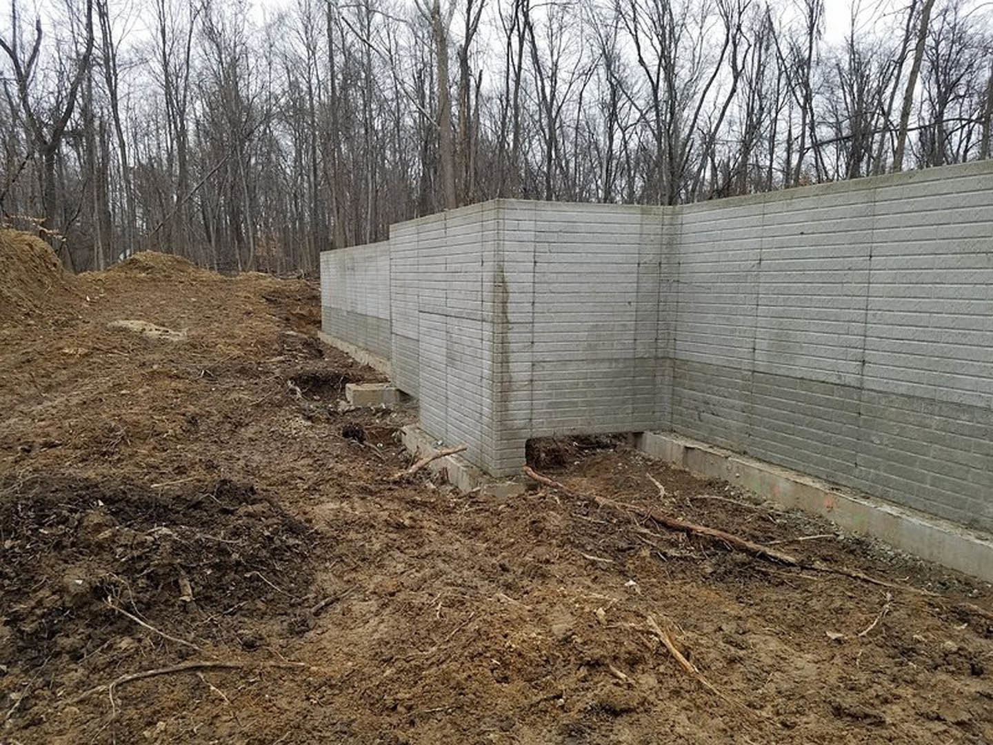 Concrete block wall with exposed soil and mature trees in the background
