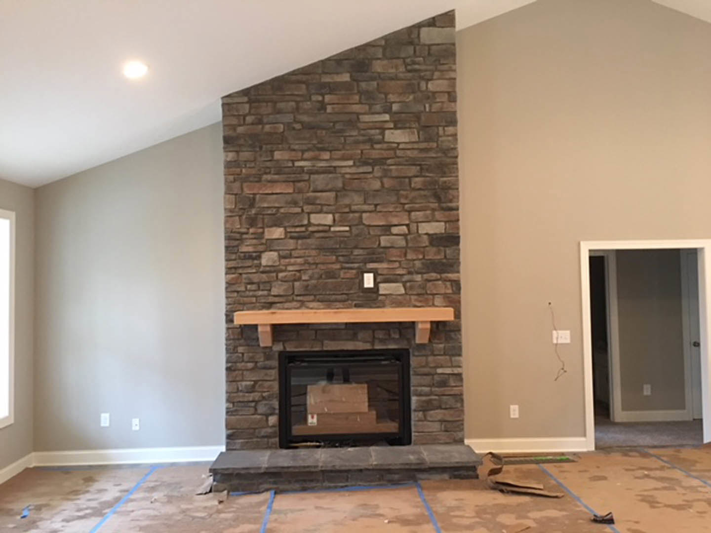 Brick fireplace with wood mantel, stacked firewood in glass case, white door with matching frame, wood plank accent on brick wall, hardwood floor