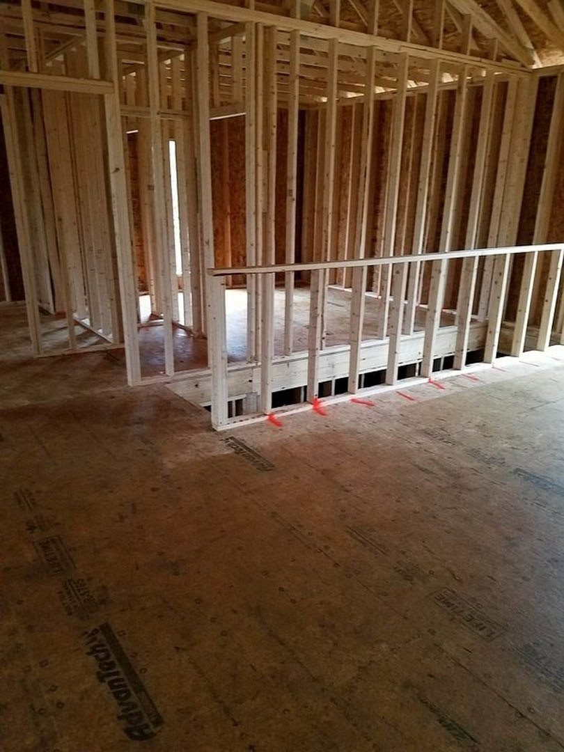 Exposed wood framing and beams in an unfinished room, plywood subfloor with red tape markings, natural brown lumber throughout interior construction.