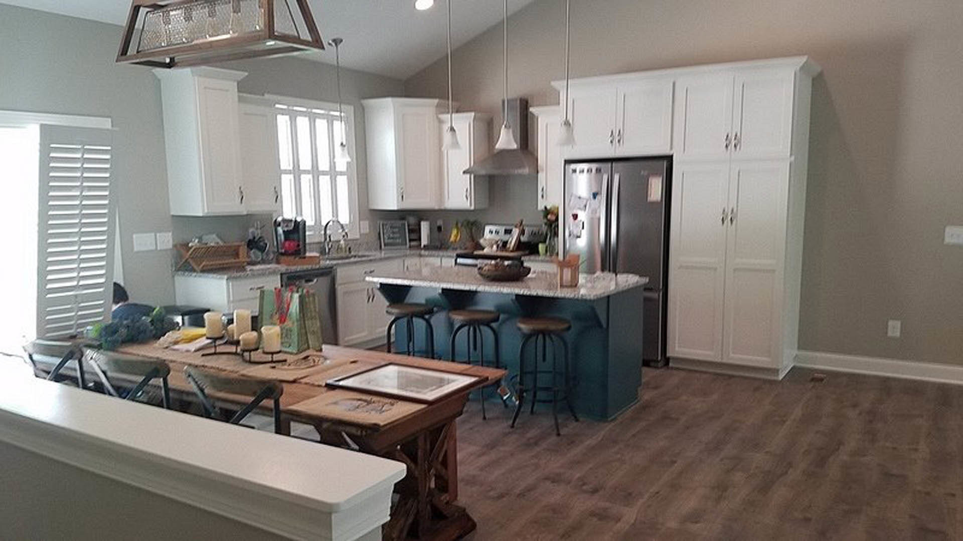 White kitchen with shaker cabinets, quartz countertops, large central island, stainless steel sink, and dining table with chairs against a white wall.
