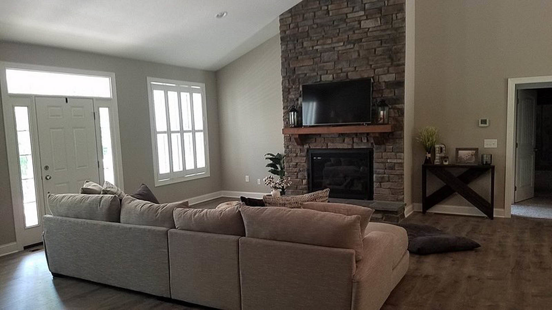 Living room with brick fireplace, gray sectional couch, hardwood floors, potted plant, and neutral walls