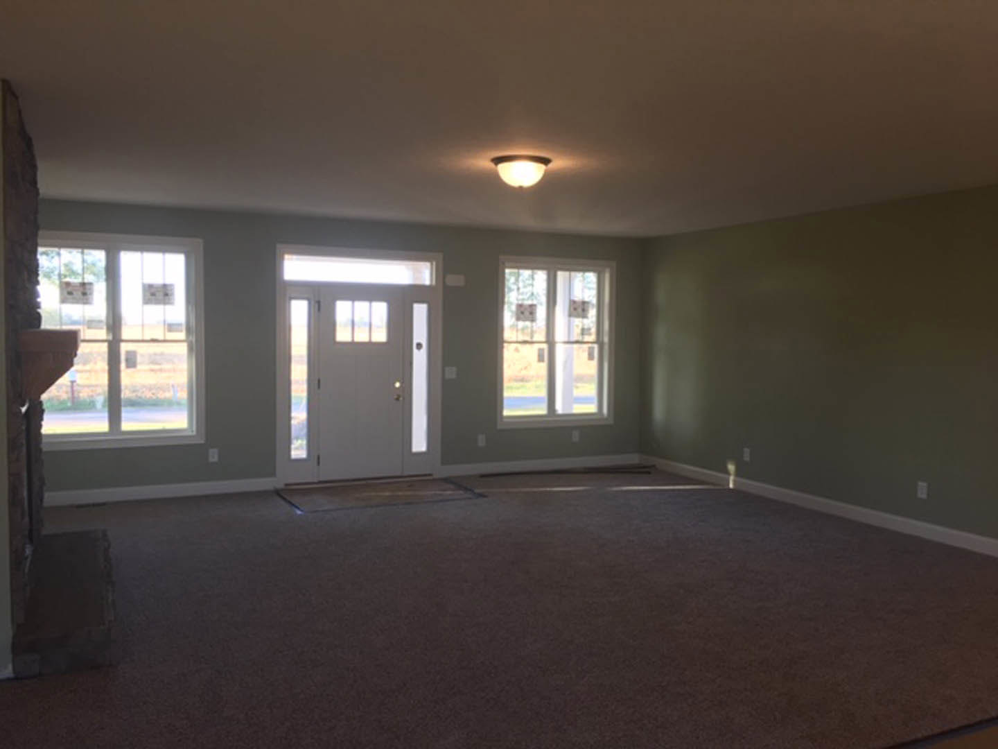 Carpeted room with white door featuring glass panes, two windows with signs, light fixture on ceiling, plaster walls and ceiling.