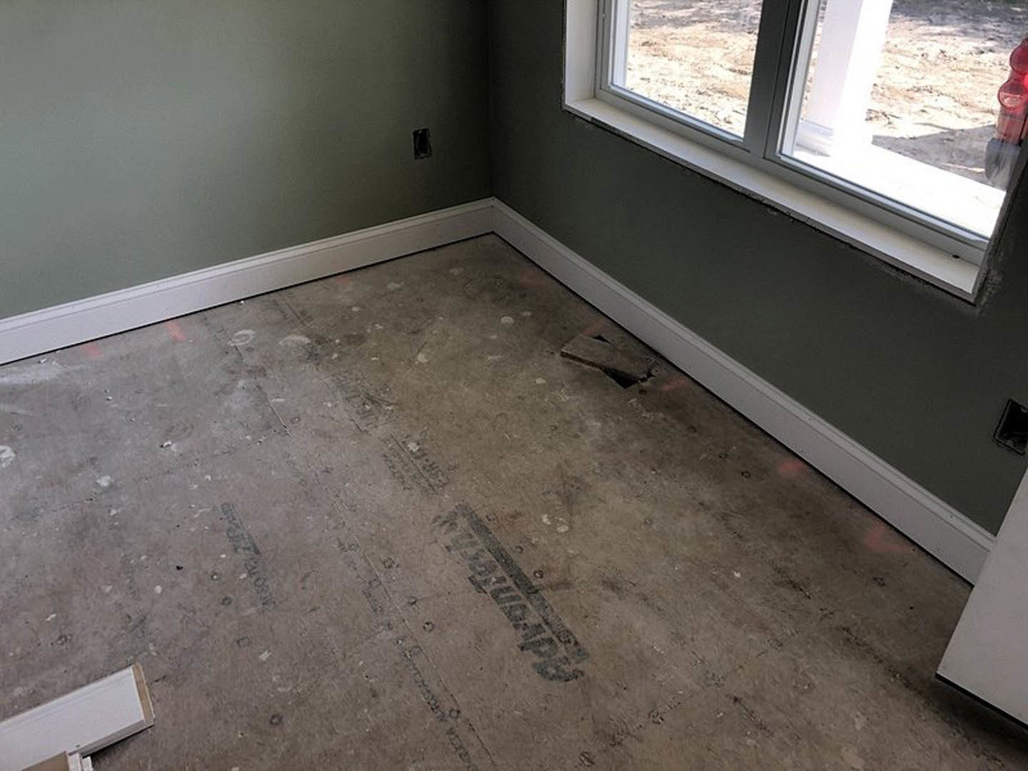 White-framed window set in plastered wall, unfinished concrete floor with visible hole, scattered construction materials