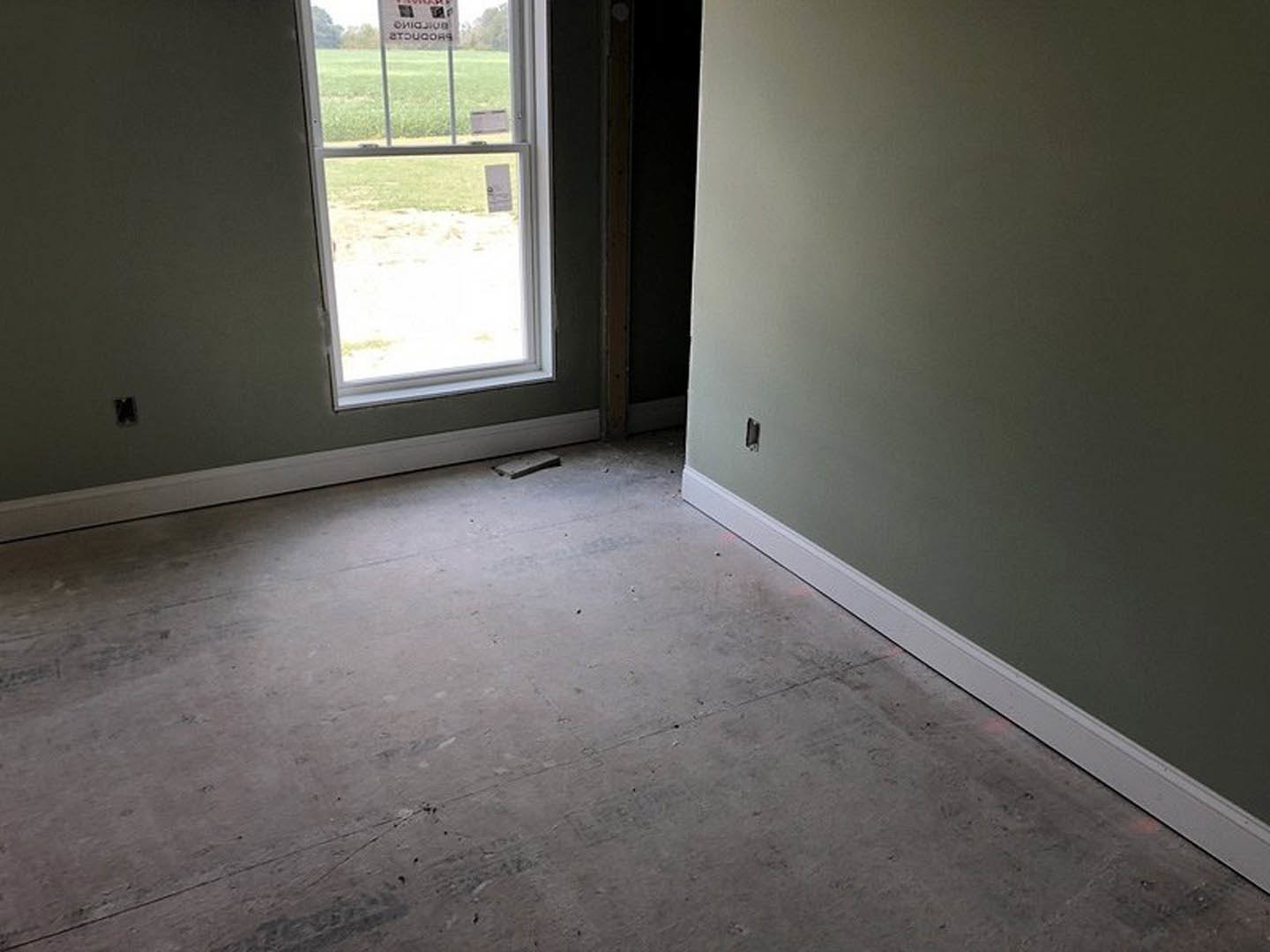 Concrete floor with white trim, plaster walls, window with a sign, daylight illuminating the room