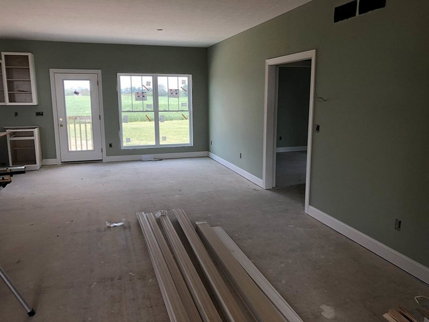 Room with light wood flooring, plaster walls, multiple windows, exposed wood ceiling beams, white shelving with wood handles, and a white door featuring a glass window.